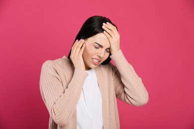 Woman suffering from migraine on pink background