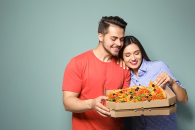 Attractive young couple with delicious pizza on color background