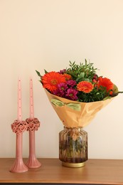 Photo of Bouquet of flowers and candles on wooden table near white wall