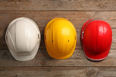 Photo of Different hard hats on wooden background, top view. Safety equipment
