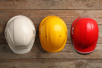 Different hard hats on wooden background, top view. Safety equipment