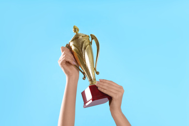 Photo of Woman holding gold trophy cup on light blue background, closeup