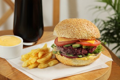 Photo of Tasty vegetarian burger served with french fries and sauce on wooden table, closeup