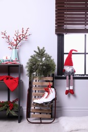 Sleigh with pair of ice skates and fir branches near window in decorated room