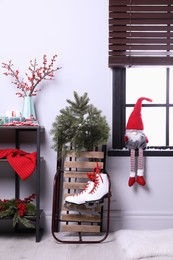 Photo of Sleigh with pair of ice skates and fir branches near window in decorated room