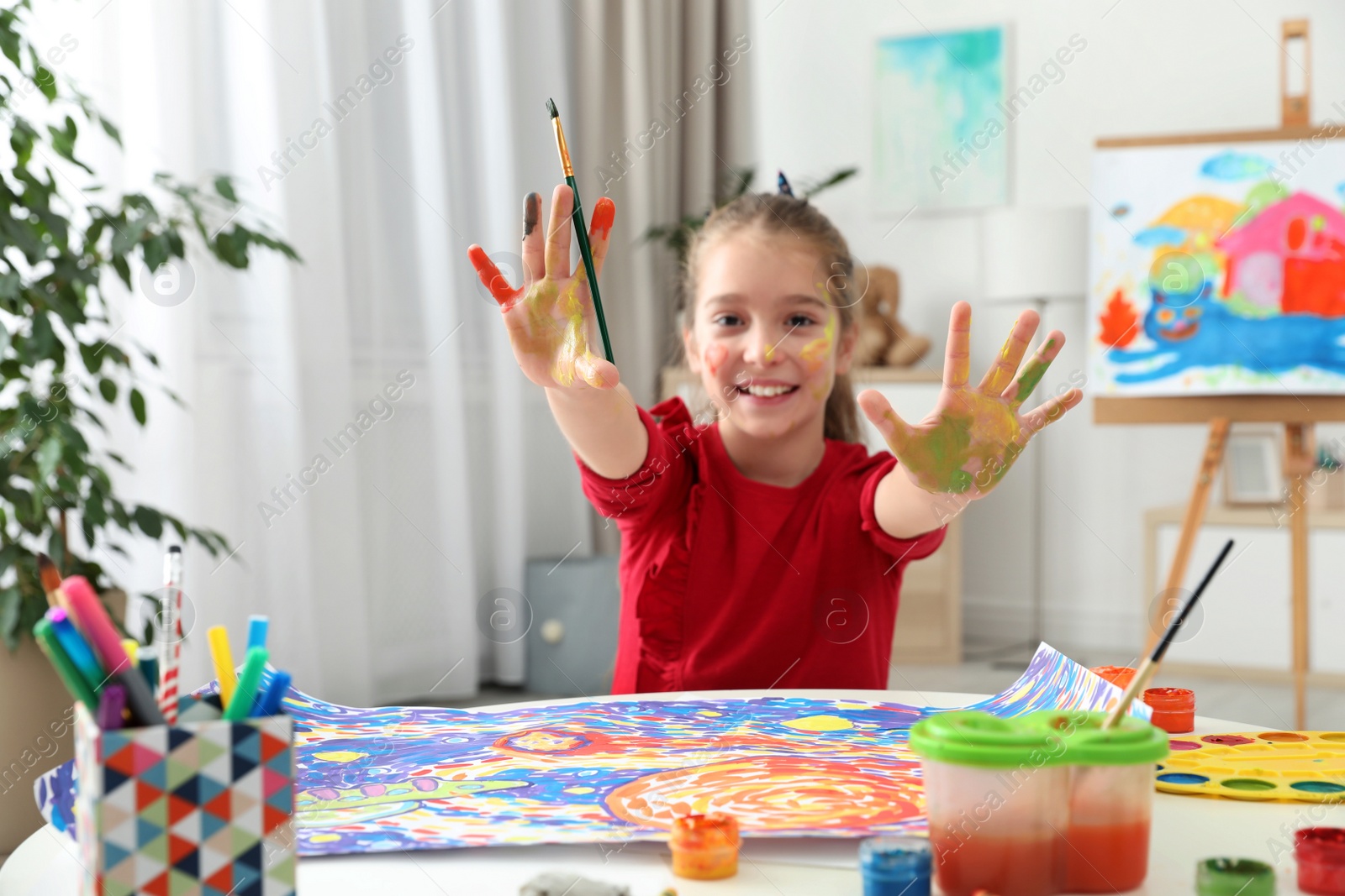 Photo of Little child with painted hands and face at table indoors