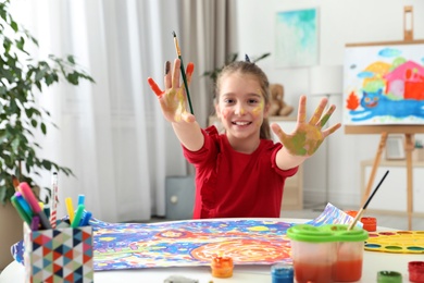 Photo of Little child with painted hands and face at table indoors