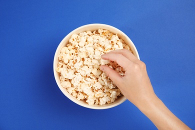 Woman with paper bucket of popcorn on color background, top view