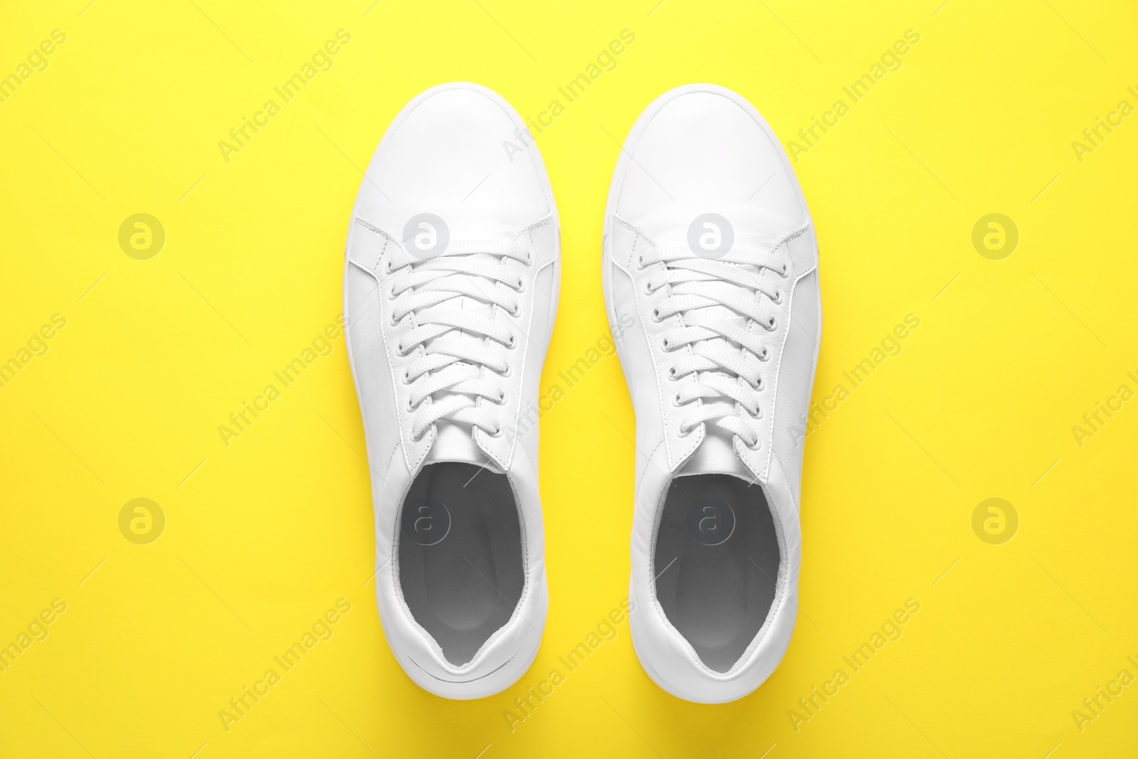 Photo of Pair of stylish white sneakers on yellow background, top view