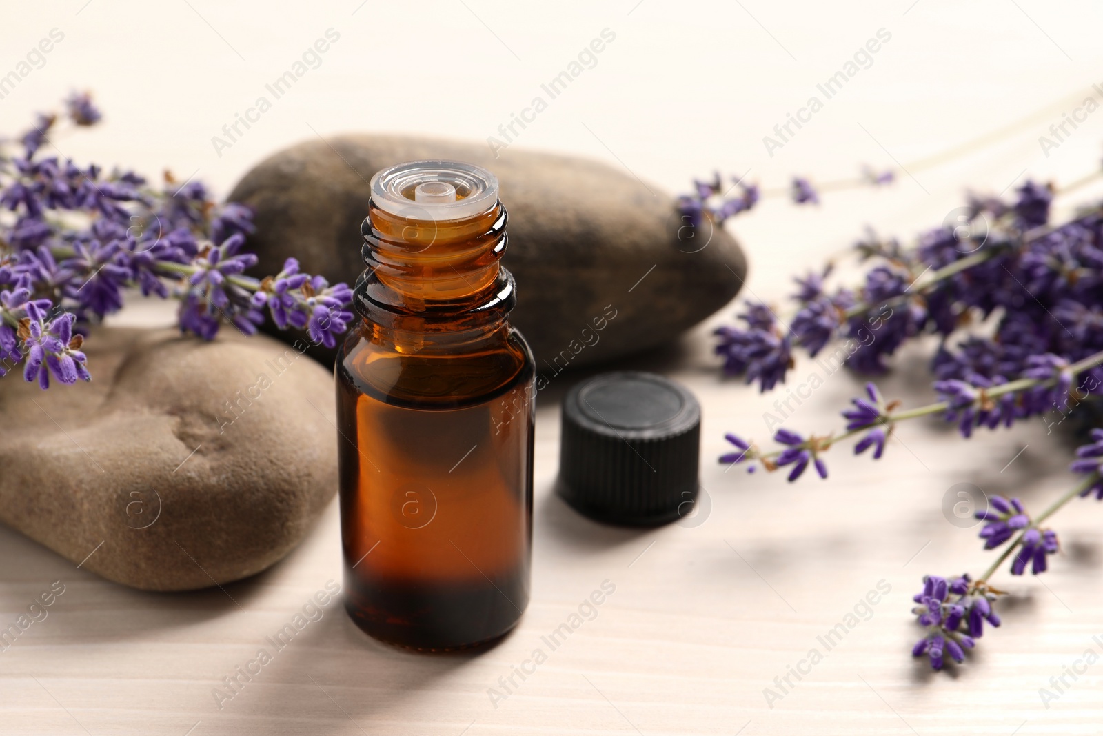 Photo of Bottle of essential oil and lavender flowers on white wooden table, closeup. Space for text