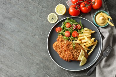 Tasty schnitzels served with potato fries, tomatoes and arugula on grey table, flat lay. Space for text