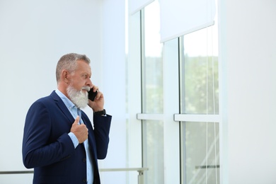 Photo of Portrait of handsome mature man in elegant suit talking on mobile phone near window