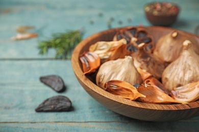 Bowl of black garlic on blue wooden table. Space for text