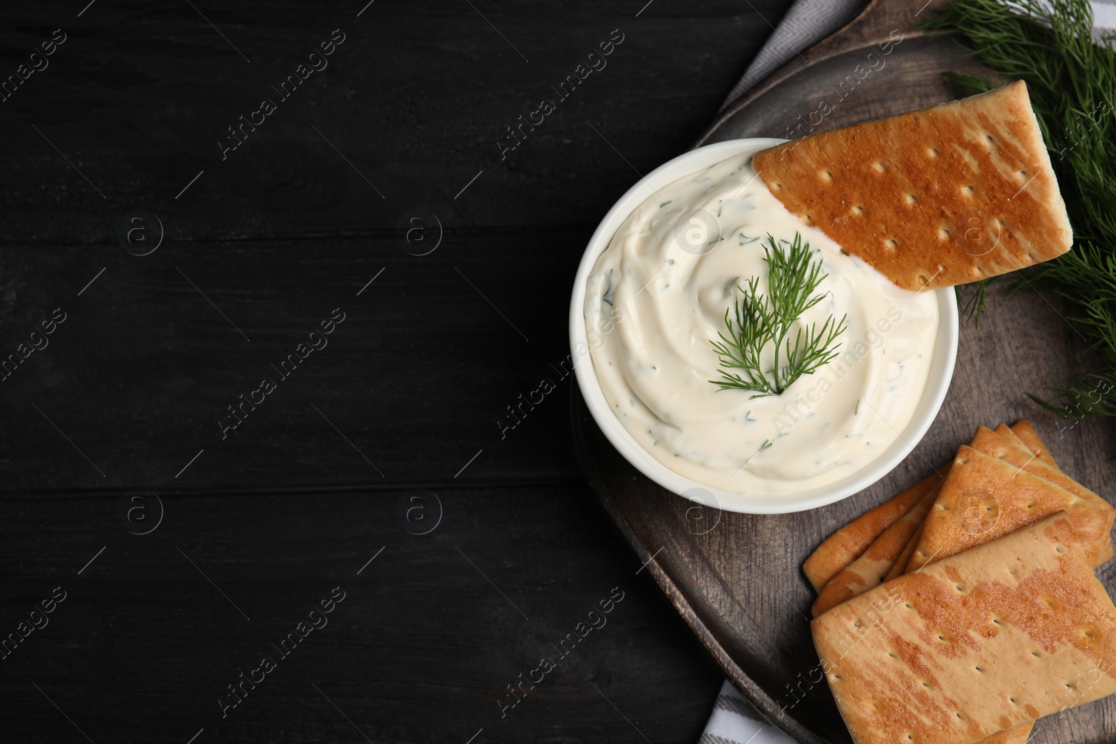 Photo of Tasty creamy dill sauce with crackers on black wooden table, flat lay. Space for text