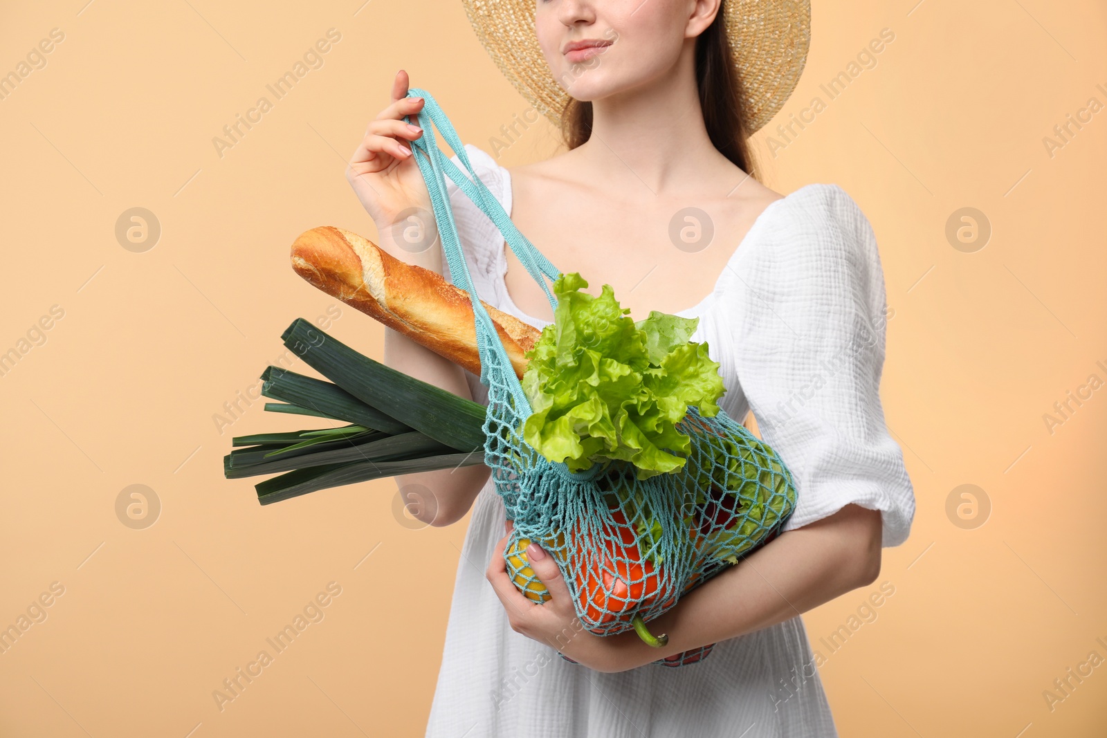 Photo of Woman with string bag of fresh vegetables and baguette on beige background, closeup