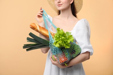 Woman with string bag of fresh vegetables and baguette on beige background, closeup