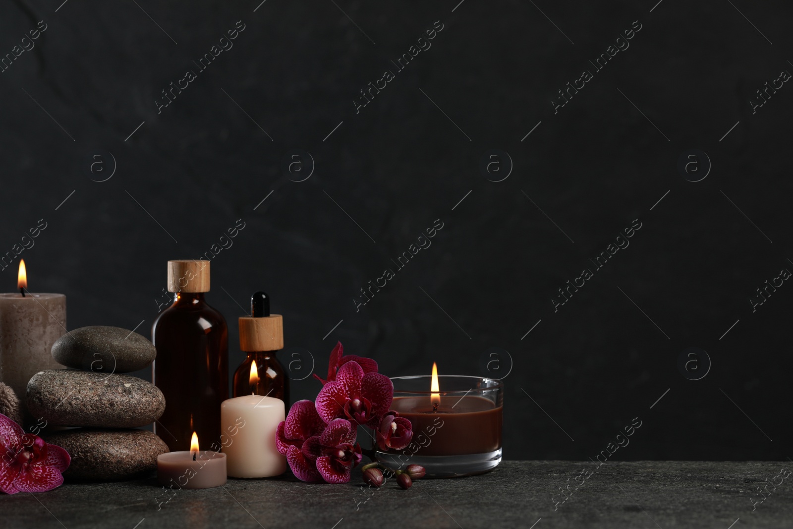 Photo of Beautiful composition with burning candles, spa stones and different care products on dark grey table. Space for text