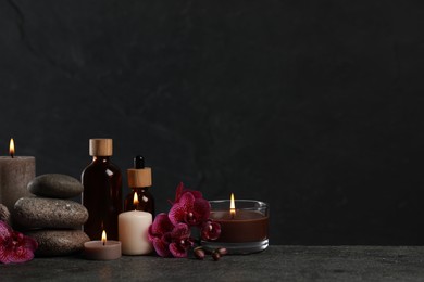 Photo of Beautiful composition with burning candles, spa stones and different care products on dark grey table. Space for text