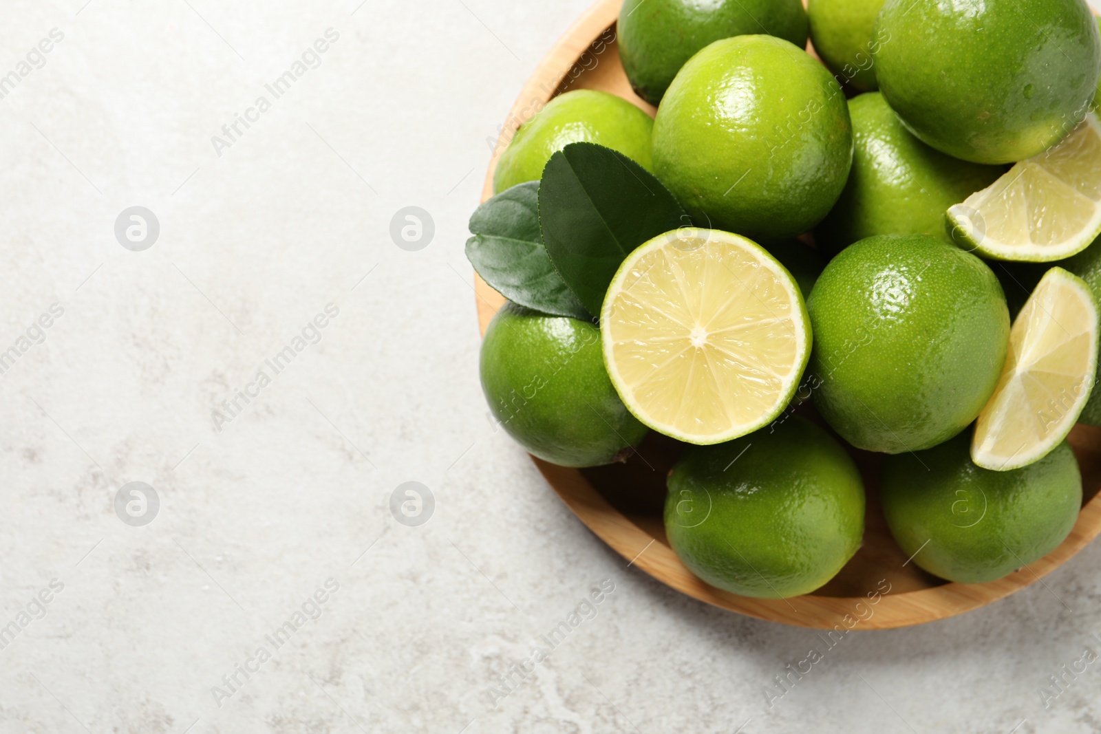 Photo of Fresh ripe limes and green leaves on light table, top view. Space for text