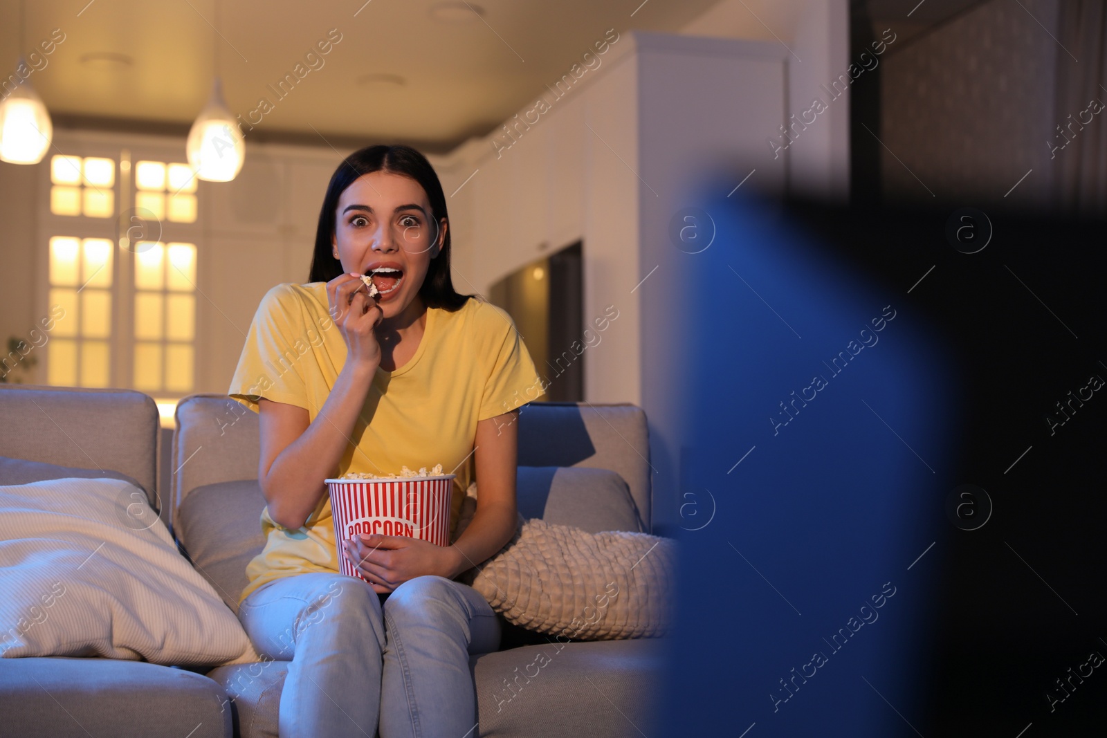 Photo of Young woman watching movie with popcorn on sofa at night