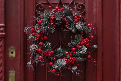 Photo of Beautiful Christmas wreath hanging on red door