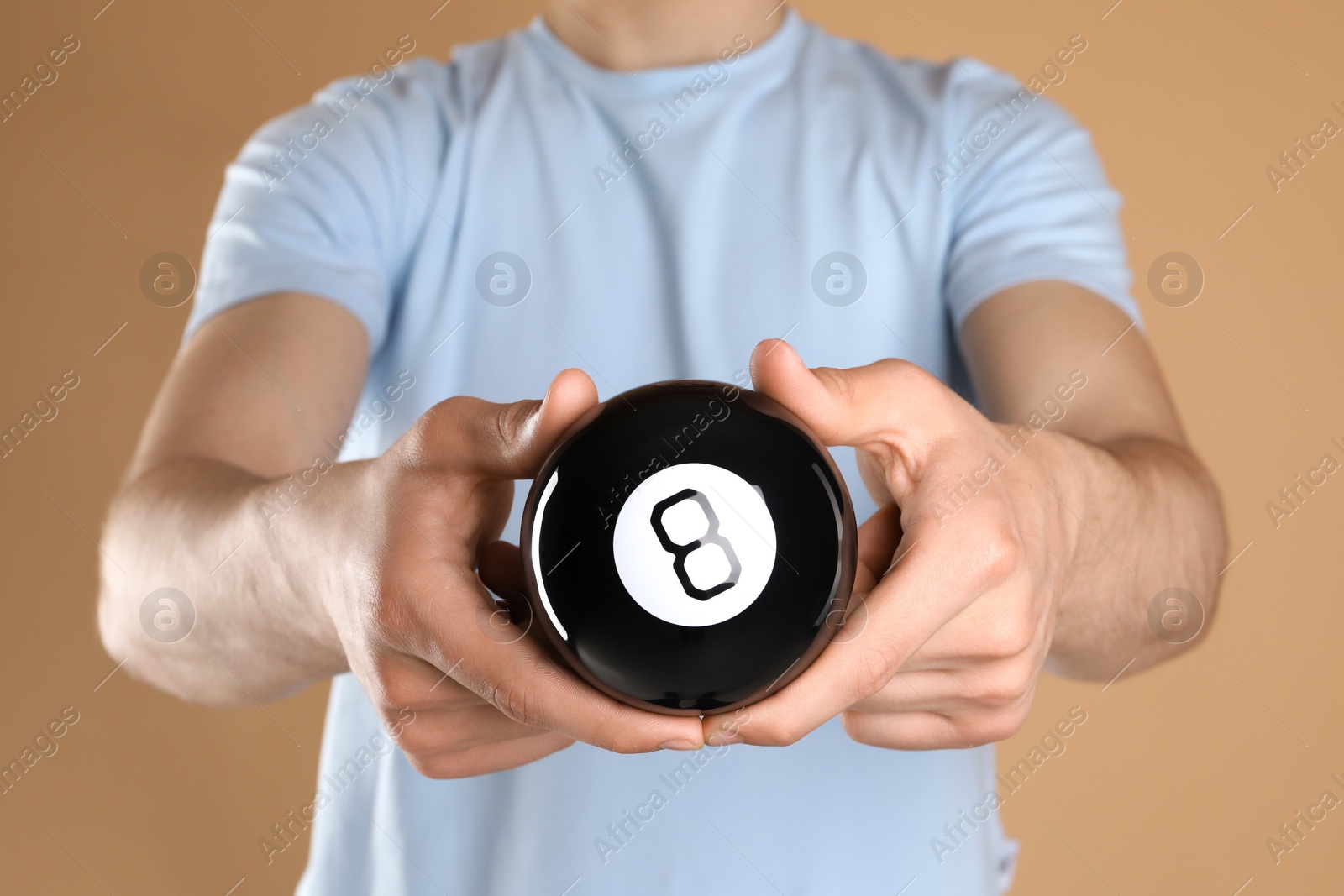 Photo of Man holding magic eight ball on light brown background, closeup