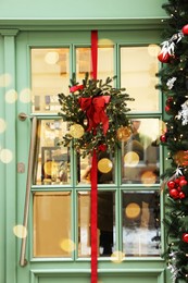 Beautiful Christmas wreath with ribbon and festive lights hanging on door