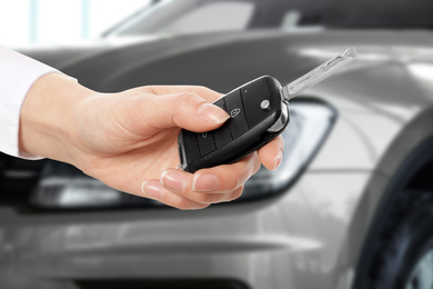 Image of Car buying. Woman holding key against blurred automobile, closeup