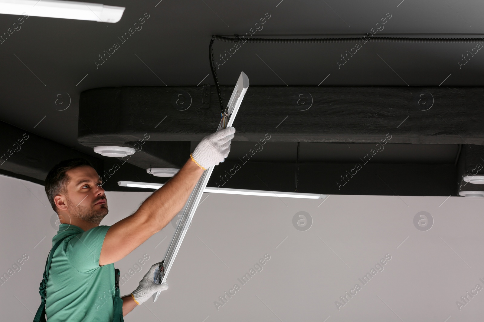 Photo of Ceiling light. Electrician installing led linear lamp indoors. Space for text