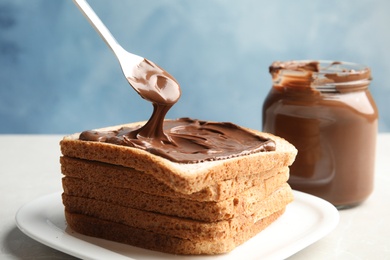 Photo of Spreading sweet chocolate cream onto toast on table against color background