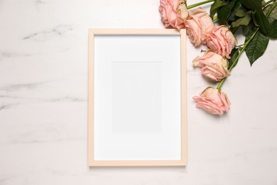 Photo of Empty photo frame and beautiful flowers on white marble background, flat lay. Space for design