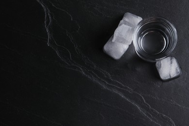 Photo of Vodka in shot glass with ice on black table, flat lay. Space for text