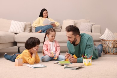 Photo of Father playing with his children while mother reading book on sofa in living room