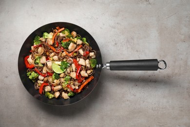 Photo of Stir-fry. Tasty noodles with meat and vegetables in wok on grey textured table, top view