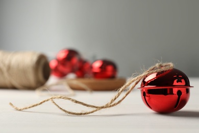 Photo of Red sleigh bell with rope on white table. Space for text