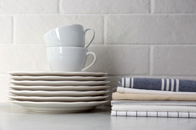 Stack of soft kitchen towels and dishware on table near white brick wall