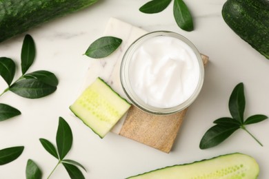 Photo of Glass jar of cucumber face cream on white marble table, flat lay