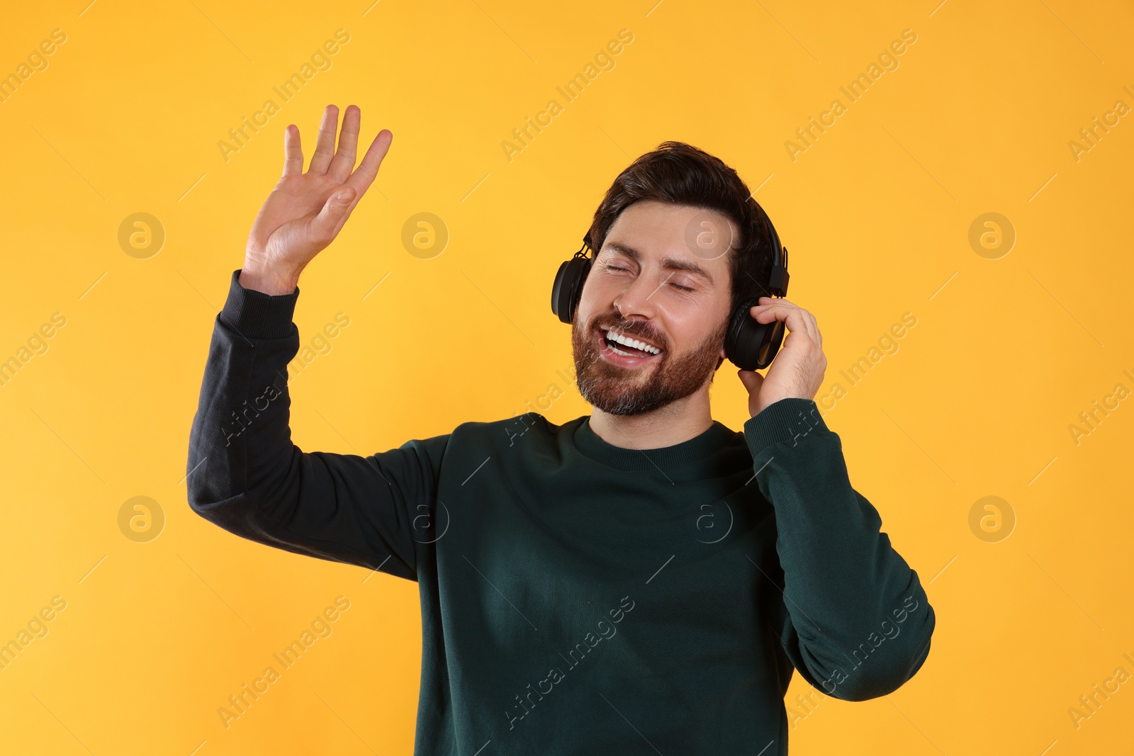 Photo of Happy man listening music with headphones on yellow background