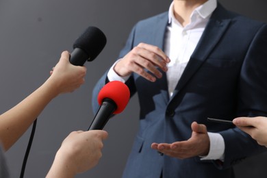 Professional journalists interviewing businessman on grey background, closeup