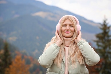Photo of Young beautiful woman wearing warm earmuffs in mountains