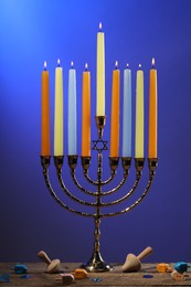 Photo of Hanukkah celebration. Menorah with burning candles and dreidels on wooden table against blue background