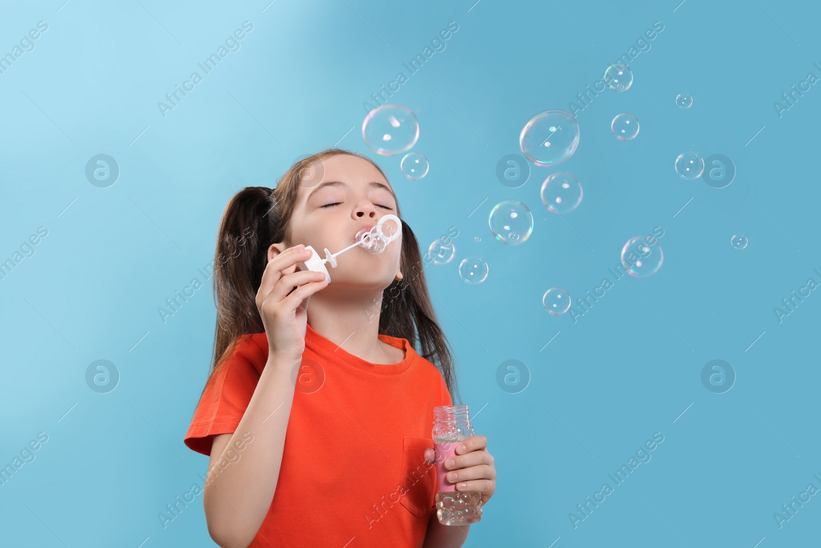 Photo of Little girl blowing soap bubbles on light blue background, space for text