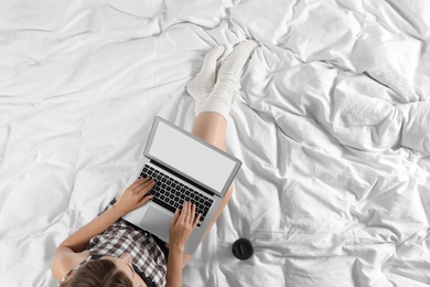 Photo of Top view of woman with laptop sitting on bed, closeup. Mockup for design