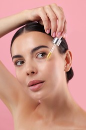 Photo of Beautiful young woman applying serum onto her face on pink background