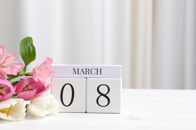 Photo of International Women's day - 8th of March. Wooden block calendar and beautiful flowers on white table, space for text