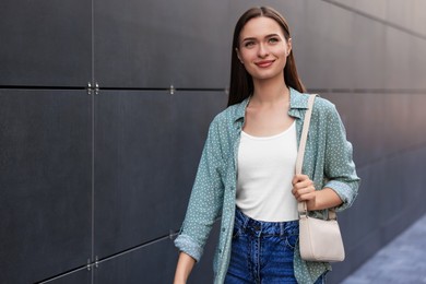 Photo of Young woman in casual clothes walking near grey wall outdoors, space for text