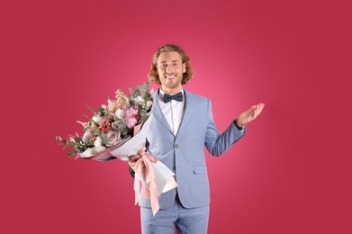 Photo of Young handsome man in stylish suit with beautiful flower bouquet on pink background