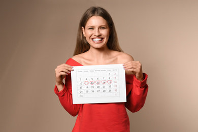Photo of Young woman holding calendar with marked menstrual cycle days on beige background