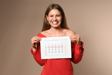 Photo of Young woman holding calendar with marked menstrual cycle days on beige background