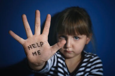 Photo of Abused little girl showing with phrase HELP ME near blue wall, focus on hand. Domestic violence concept